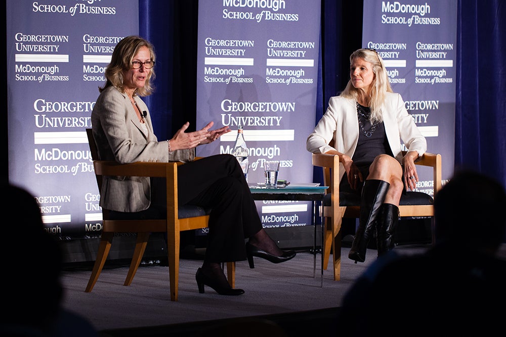 Ann Sarnoff at left addresses the audience during a public discussion event with Cathy Tinsley at right in front of a Georgetown University McDonough School of Business background.