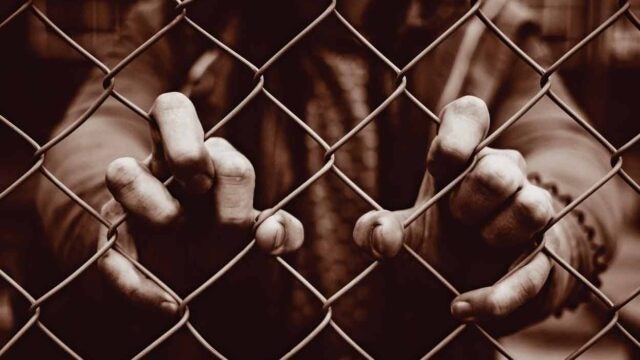 person putting fingers thru chainlink fence