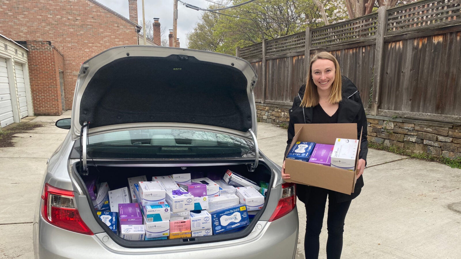 Student stands by car filled with supplies for donation