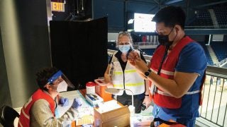 Dr. Ranit Mishori (center), medical director at the COVID-19 high-capacity vaccination site at D.C.’s Entertainment and Sports Arena, observes as Leon Padil- lia, nurse for MedStar Georgetown Student Health Center, instructs a medical student on how to prepare a dose of COVID-19 vaccine.