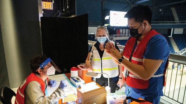 Dr. Ranit Mishori (center), medical director at the COVID-19 high-capacity vaccination site at D.C.’s Entertainment and Sports Arena, observes as Leon Padil- lia, nurse for MedStar Georgetown Student Health Center, instructs a medical student on how to prepare a dose of COVID-19 vaccine.