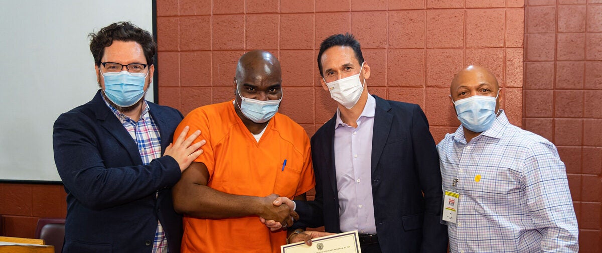 Joshua Miller (left), director of education for the Prisons and Justice Initiative and managing director for the Georgetown Pivot Program, and Marc Howard (right), director of the Prisons and Justice Initiative, celebrate Georgetown Prison Scholar Jean Remarque, who received a certificate for completing the the Fall 2021 semester at the D.C. Jail.