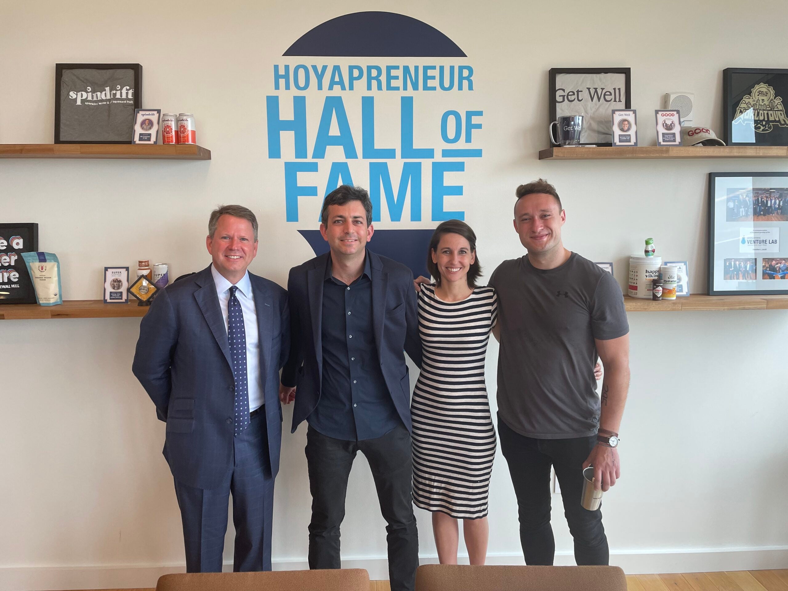 Michael Brown, Emily Owen, Etai Mizrav, and Mackenzie Copley stand in the Georgetown Vanture Lab in front of a wall reading “Hoyapreneur Hall of Fame.”