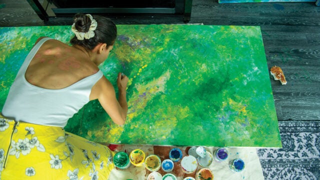 a woman in a yellow skirt paints a green abstract painting