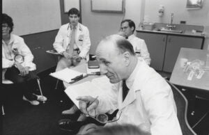 a man does a medical procedure while students watch (black and white photo)