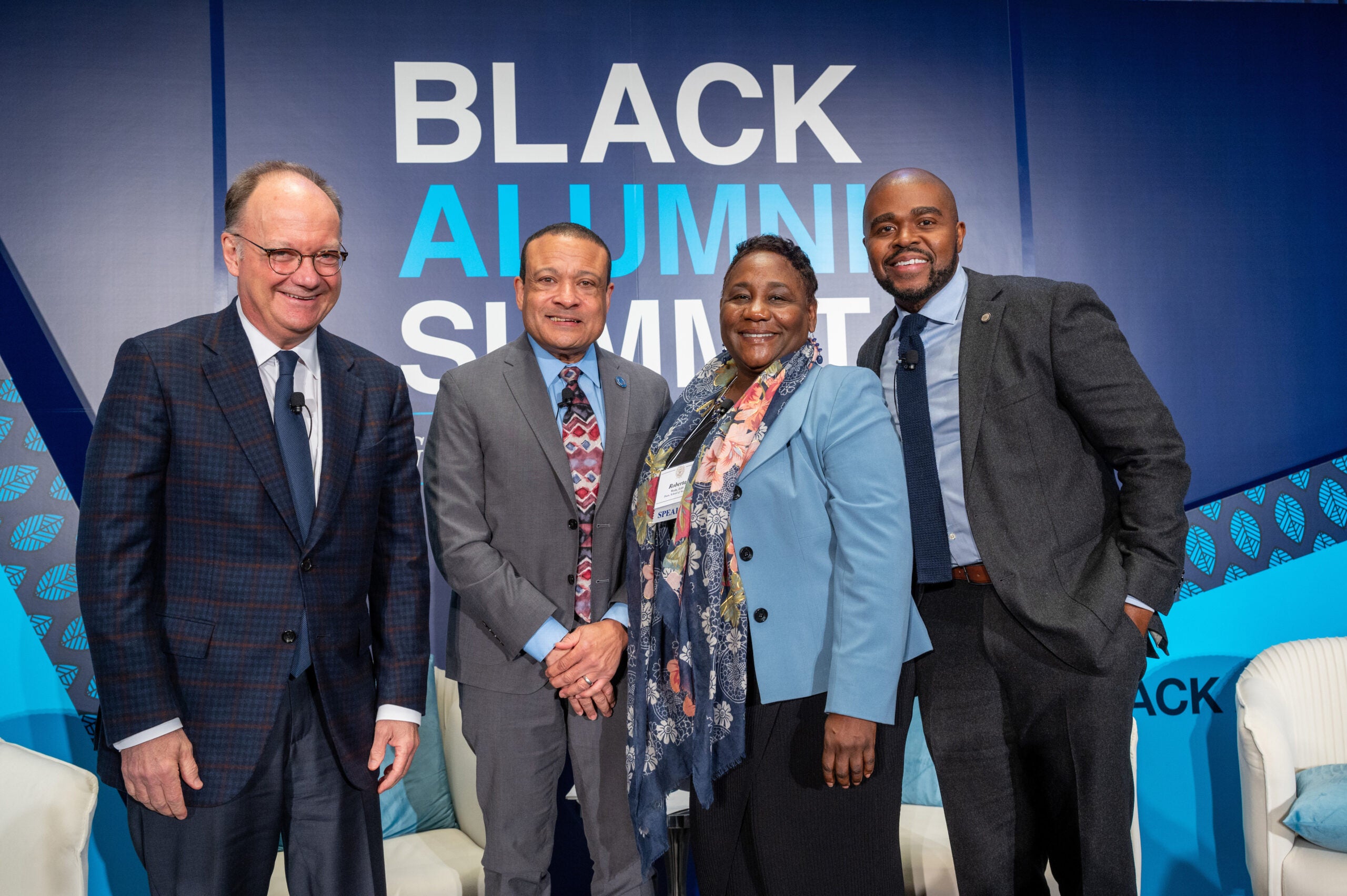four people stand next to each other with the word "Black Alumni Summit" behind them
