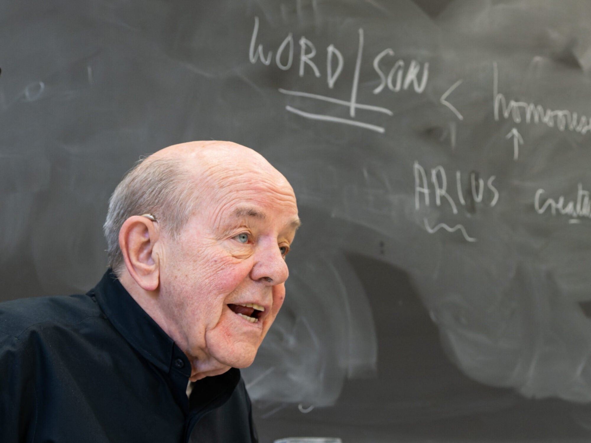 a priest stands in front of a chalkboard