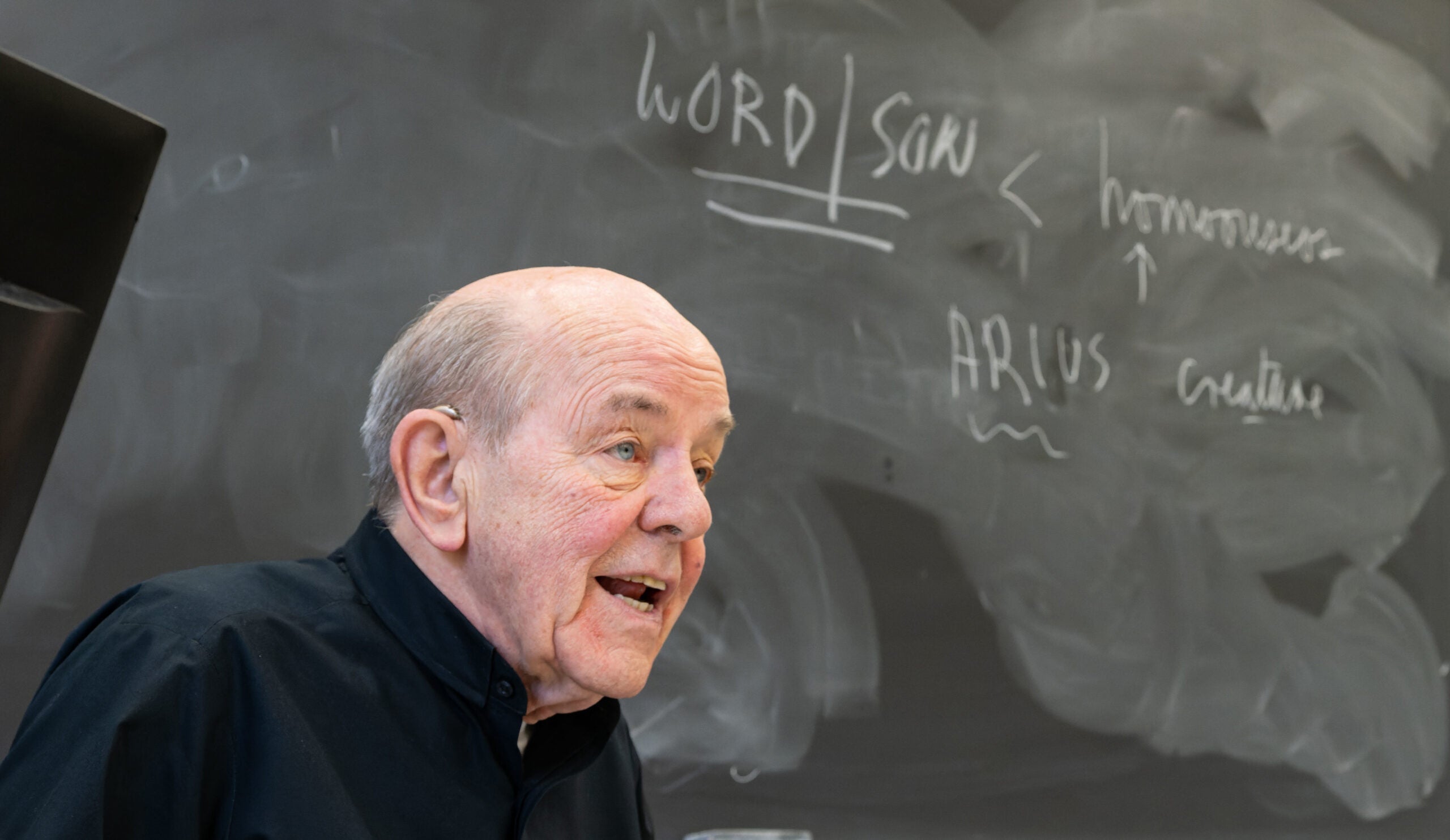 a priest stands in front of a chalkboard