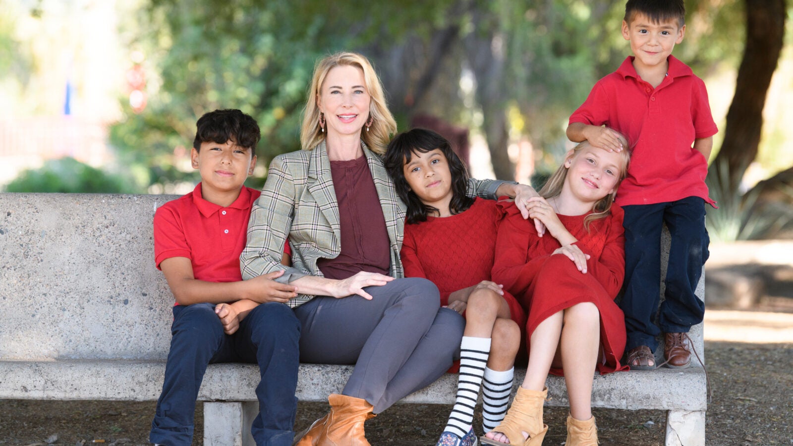 a woman sits on a bench with four children, all wearing red