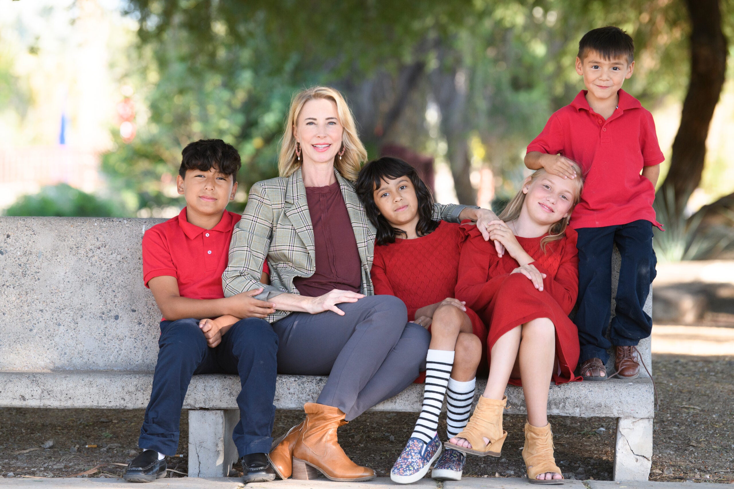 a woman sits on a bench with four children, all wearing red