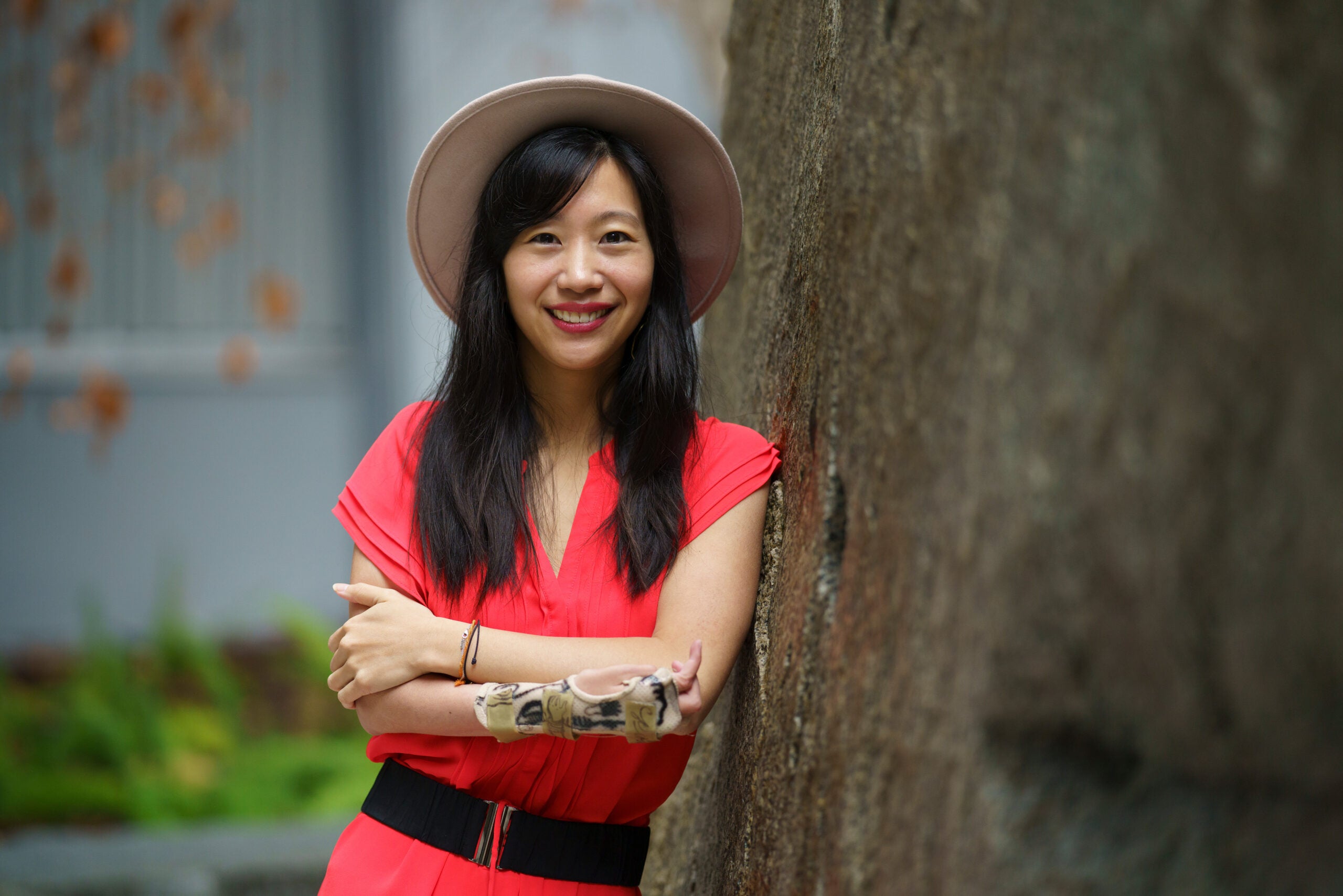 a woman next to a tree in a hat and tangerine shirt 