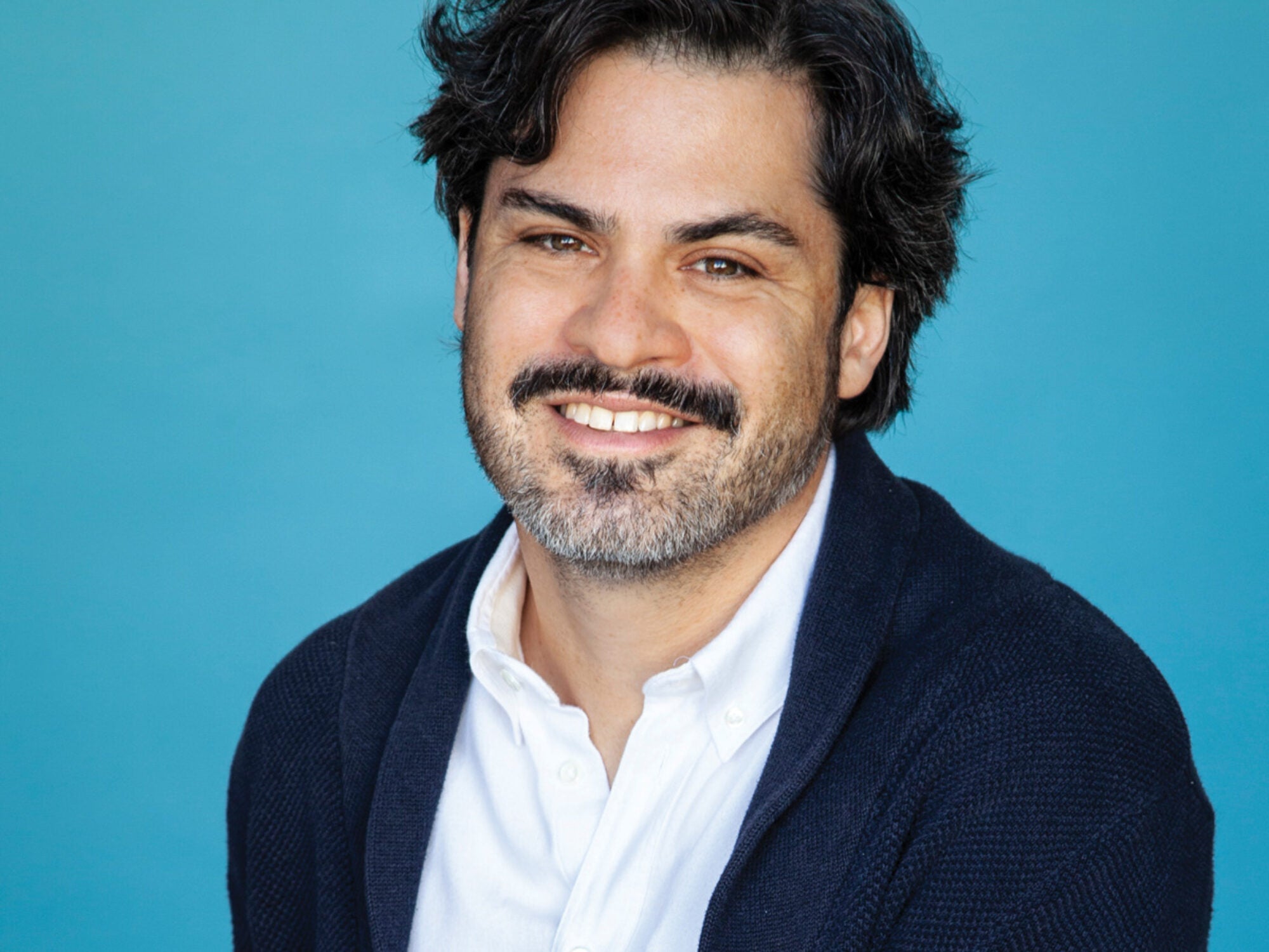 a man in a dark sweater against a teal background