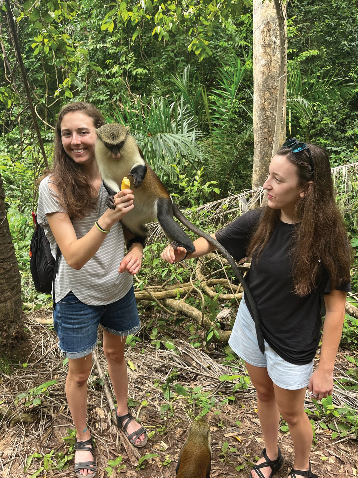 two women hold a monkey in a jungle