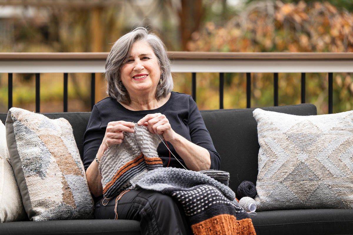 a woman sits on a deck and knits
