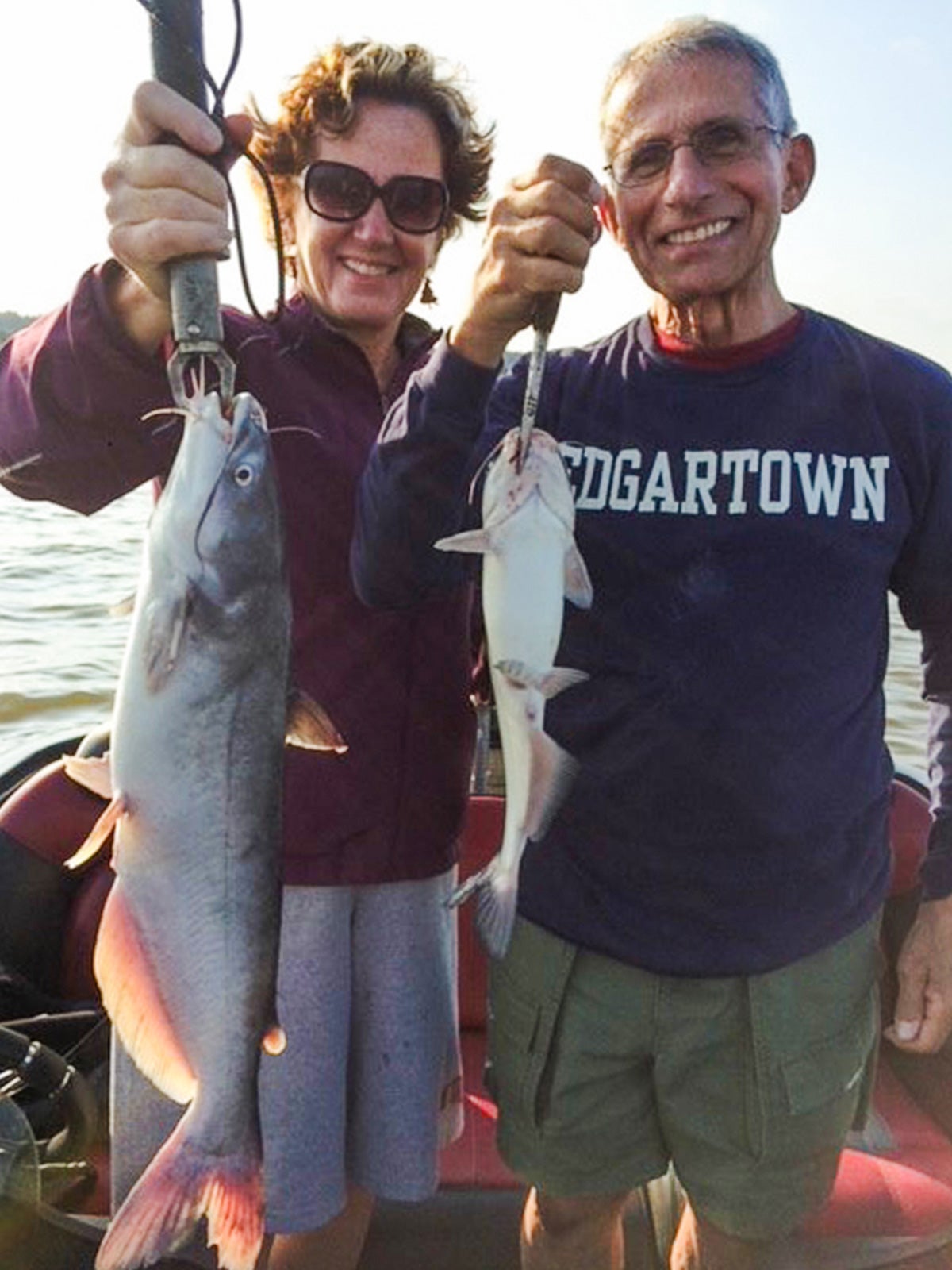 a man and a woman pose on a boat with their fish on a line