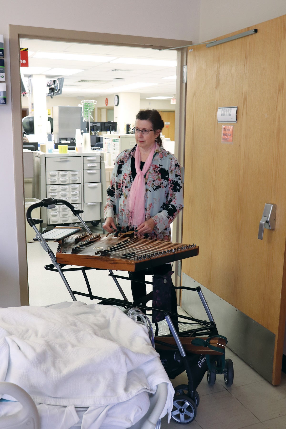a woman with a pink scarf plays a musical instrument in a hospital room