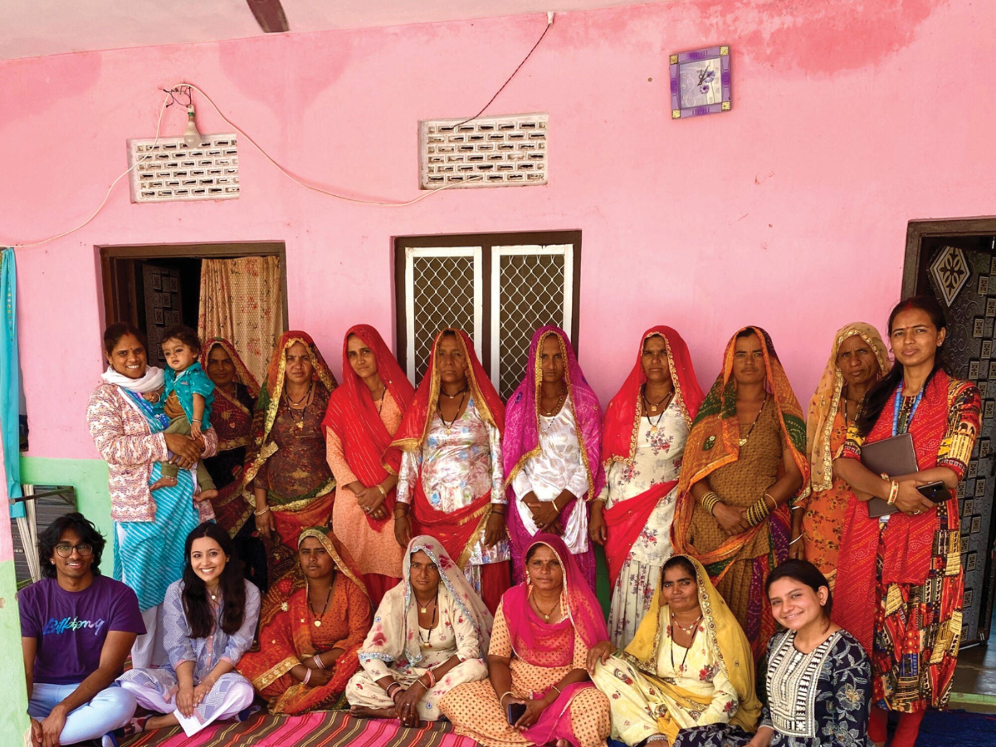women in traditional Indian saris stand in a pink room