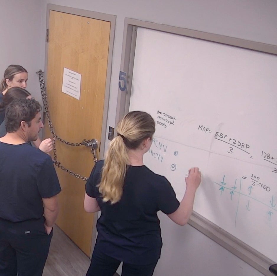three people in medical scrubs write on a whiteboard