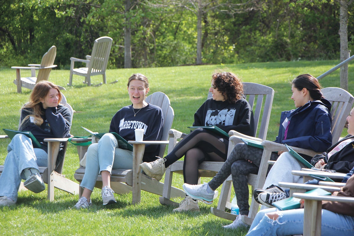students wearing Hoya and Georgetown sweatshirts sit in adirondack chairs on a wide green lawn