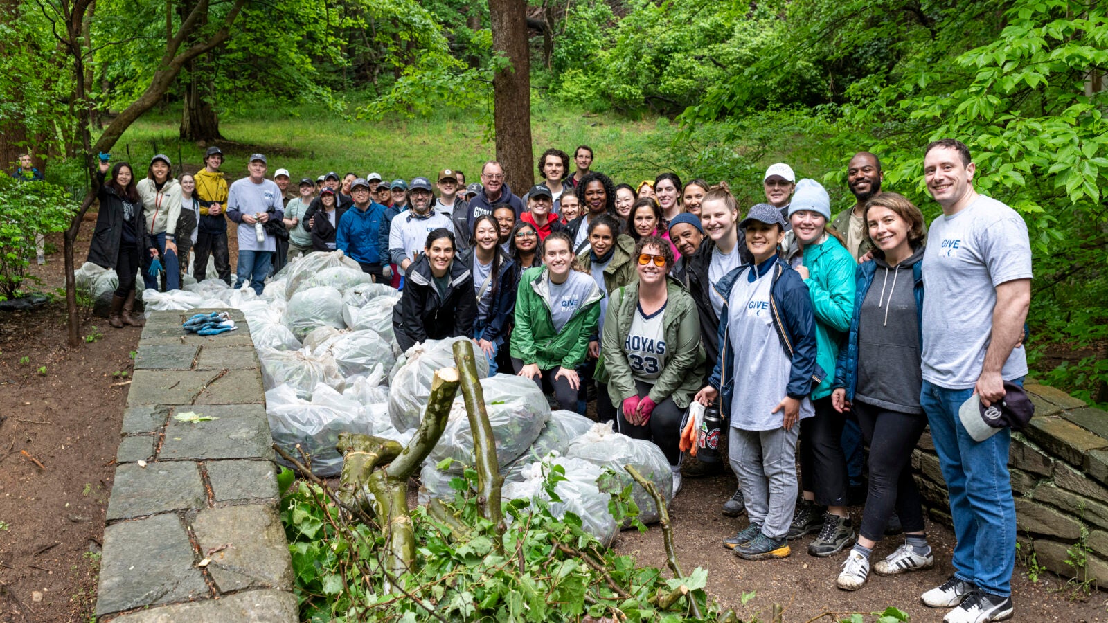 a group of people stand on a hiking trail with a pile of trash bags and branches