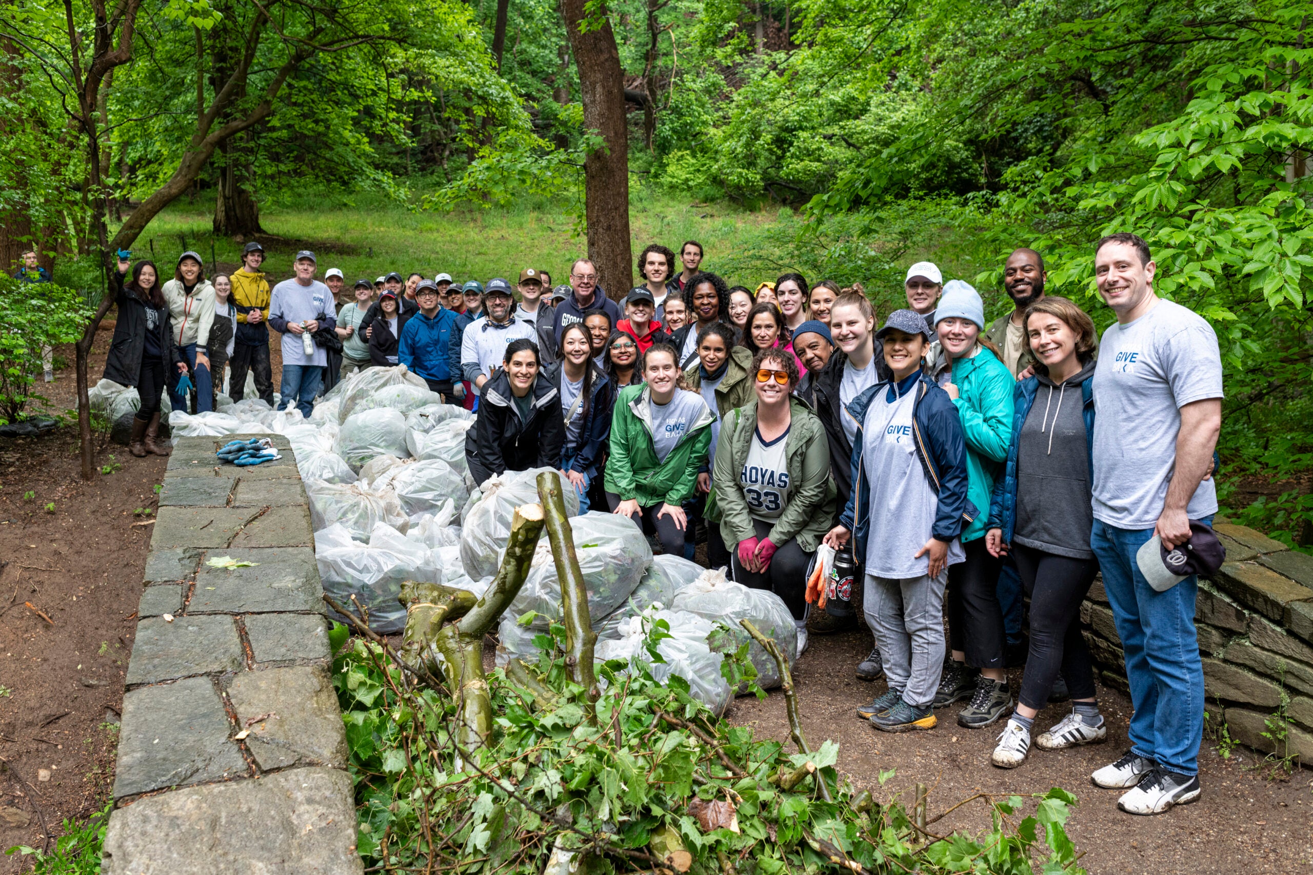 a group of people stand on a hiking trail with a pile of trash bags and branches