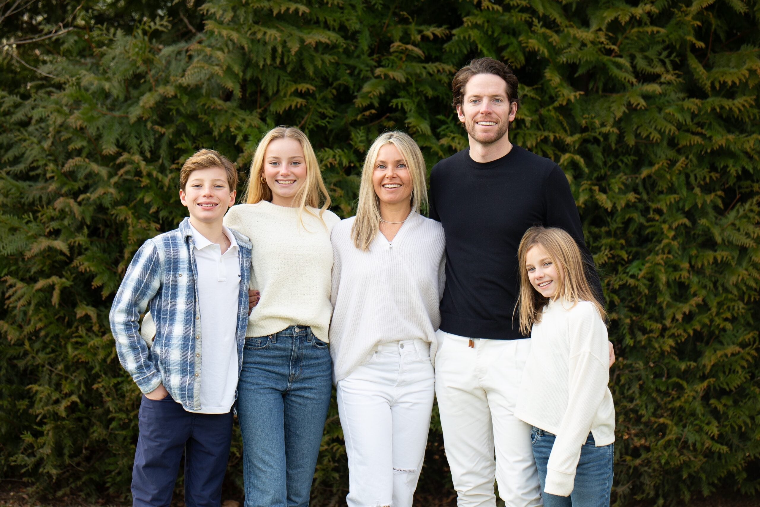 two parents and three kids pose together in front of a plant background