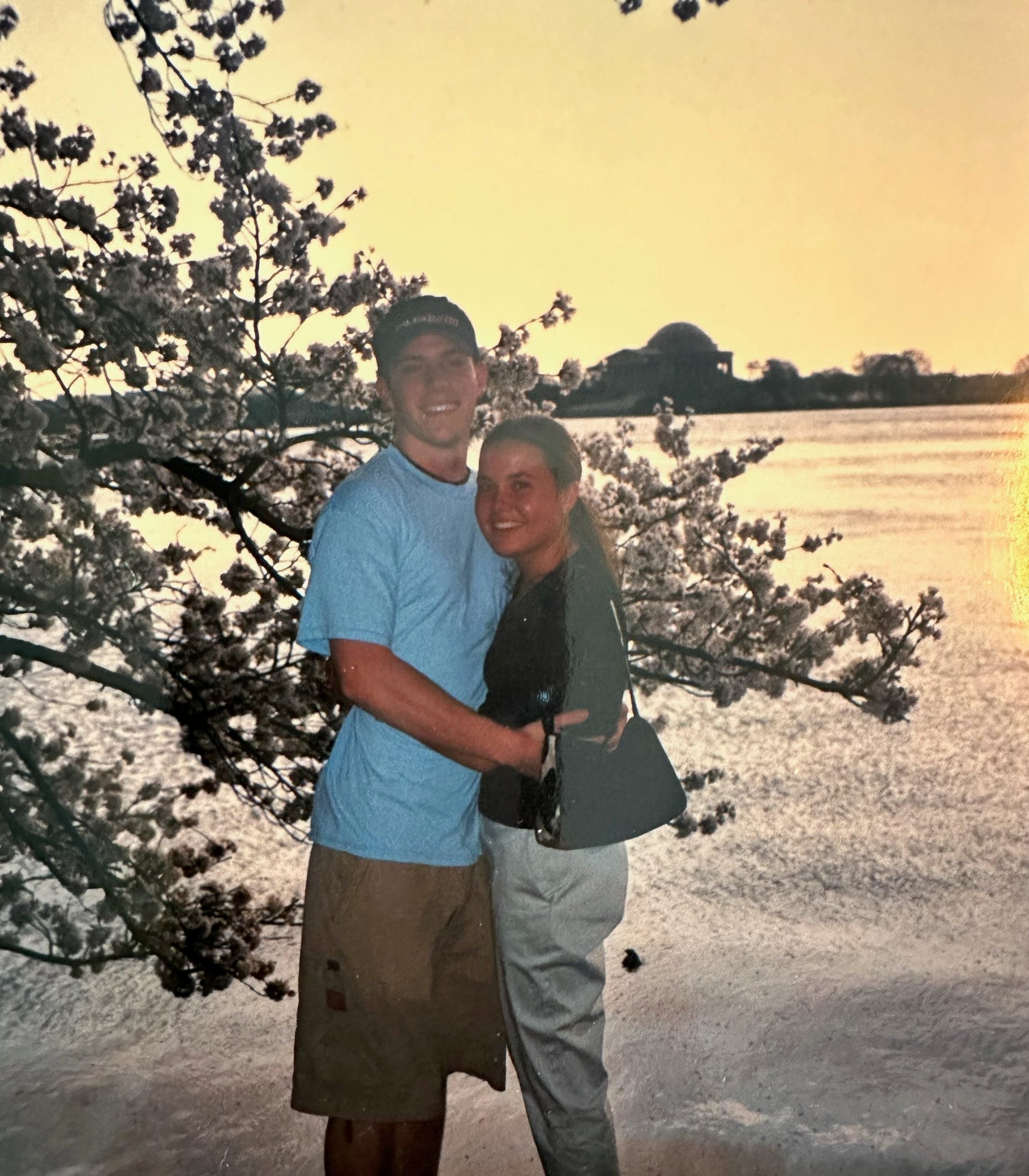 two people smile in front of a lake and tree