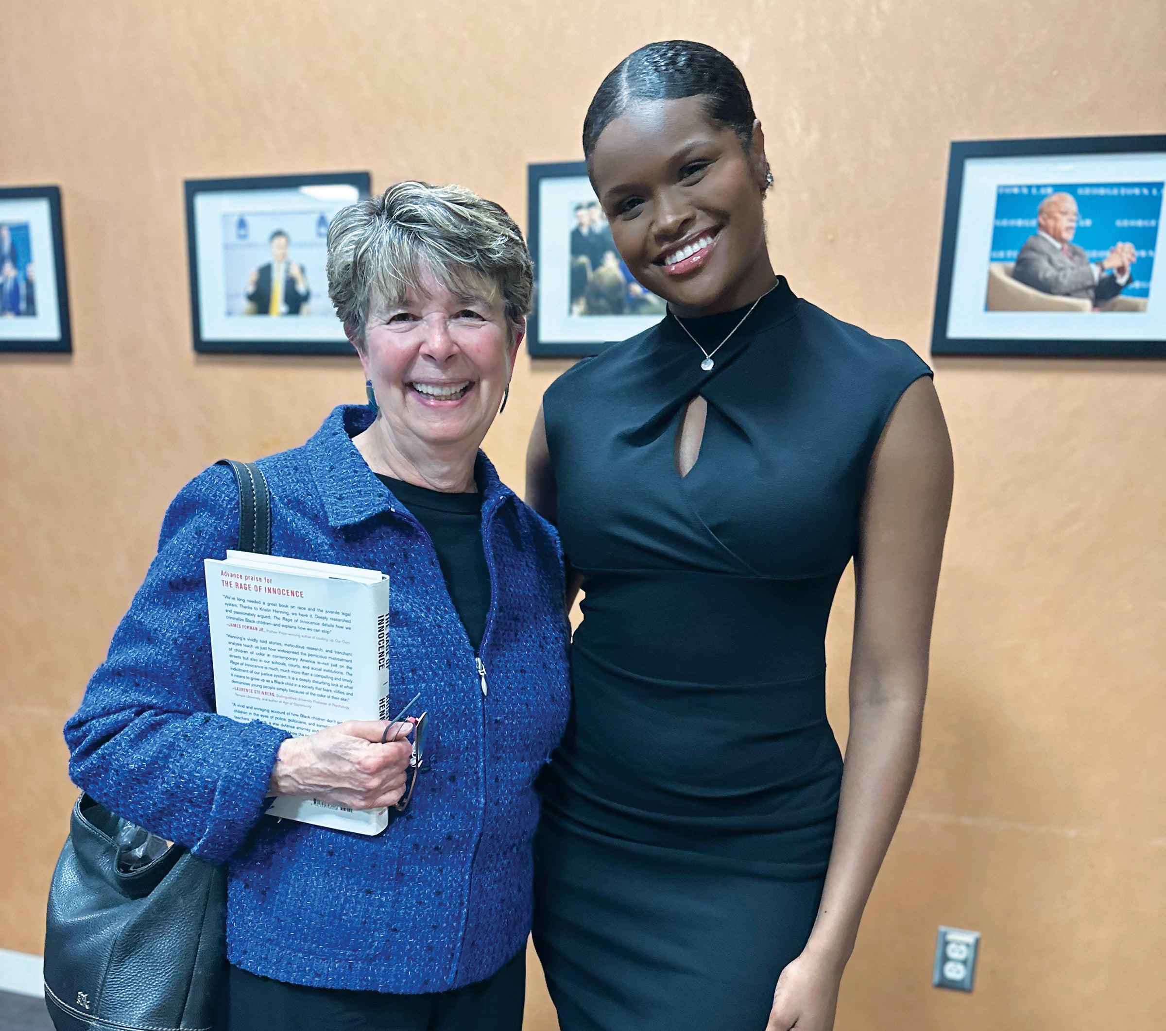 two women - one in a black dress and the other in a blue sweater - stand with each other