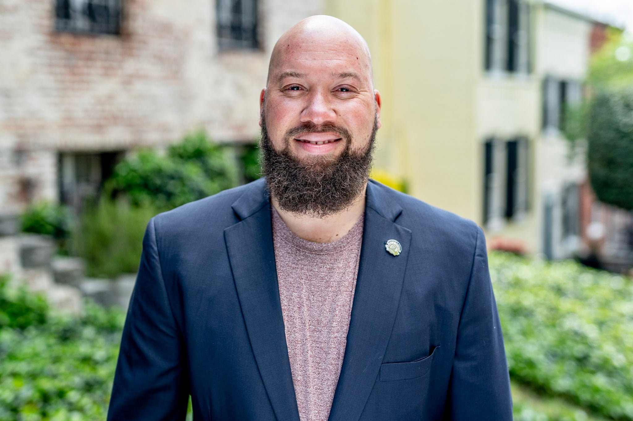 a man in a navy blazer stands in front of rowhouses