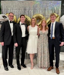 five people, two women and three men, stand in formalwear