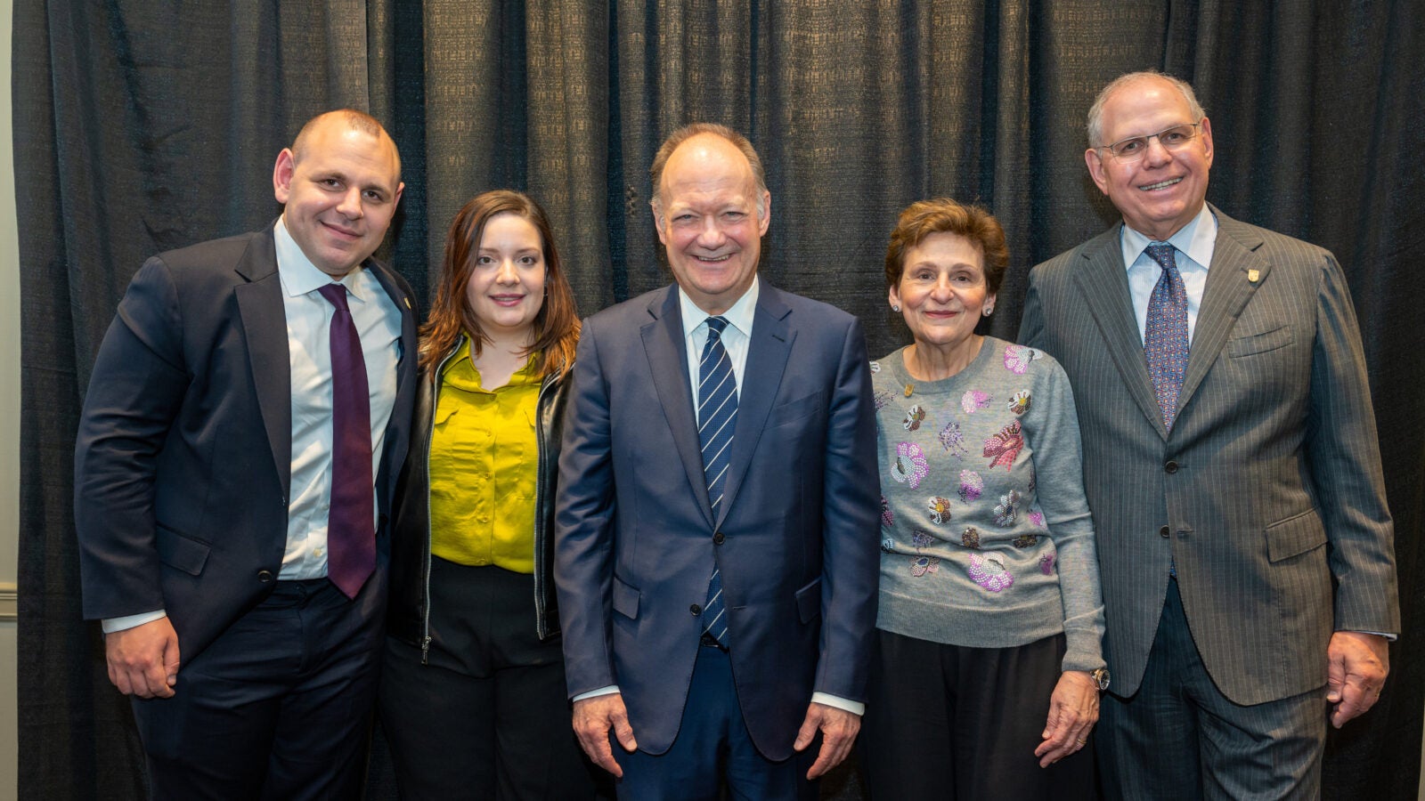 five people (three men, two women) stand together in formalwear.