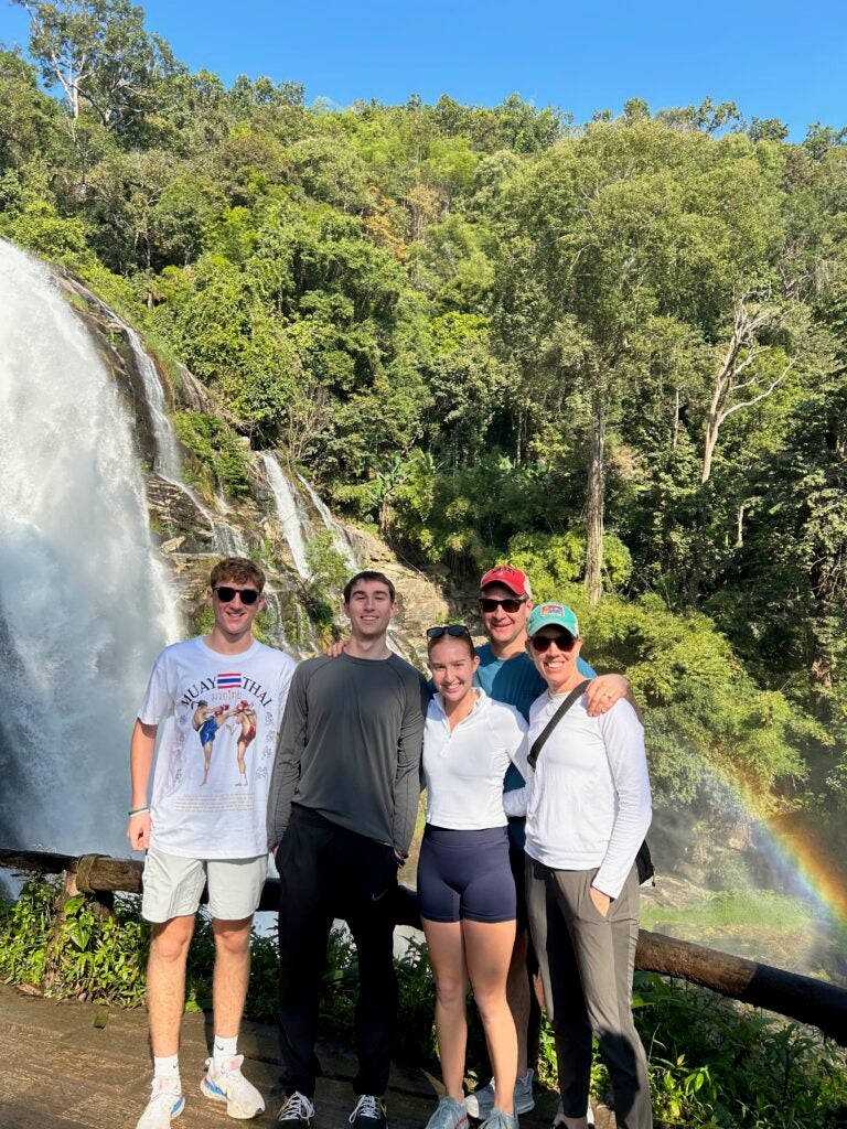 a group of five people, two women and three men, stand near a waterfall. 