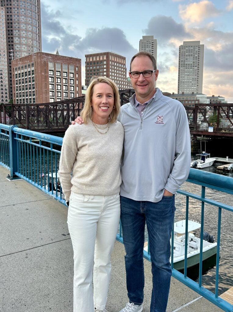 two people stand on a blue bridge in front of a city skyline in the evening