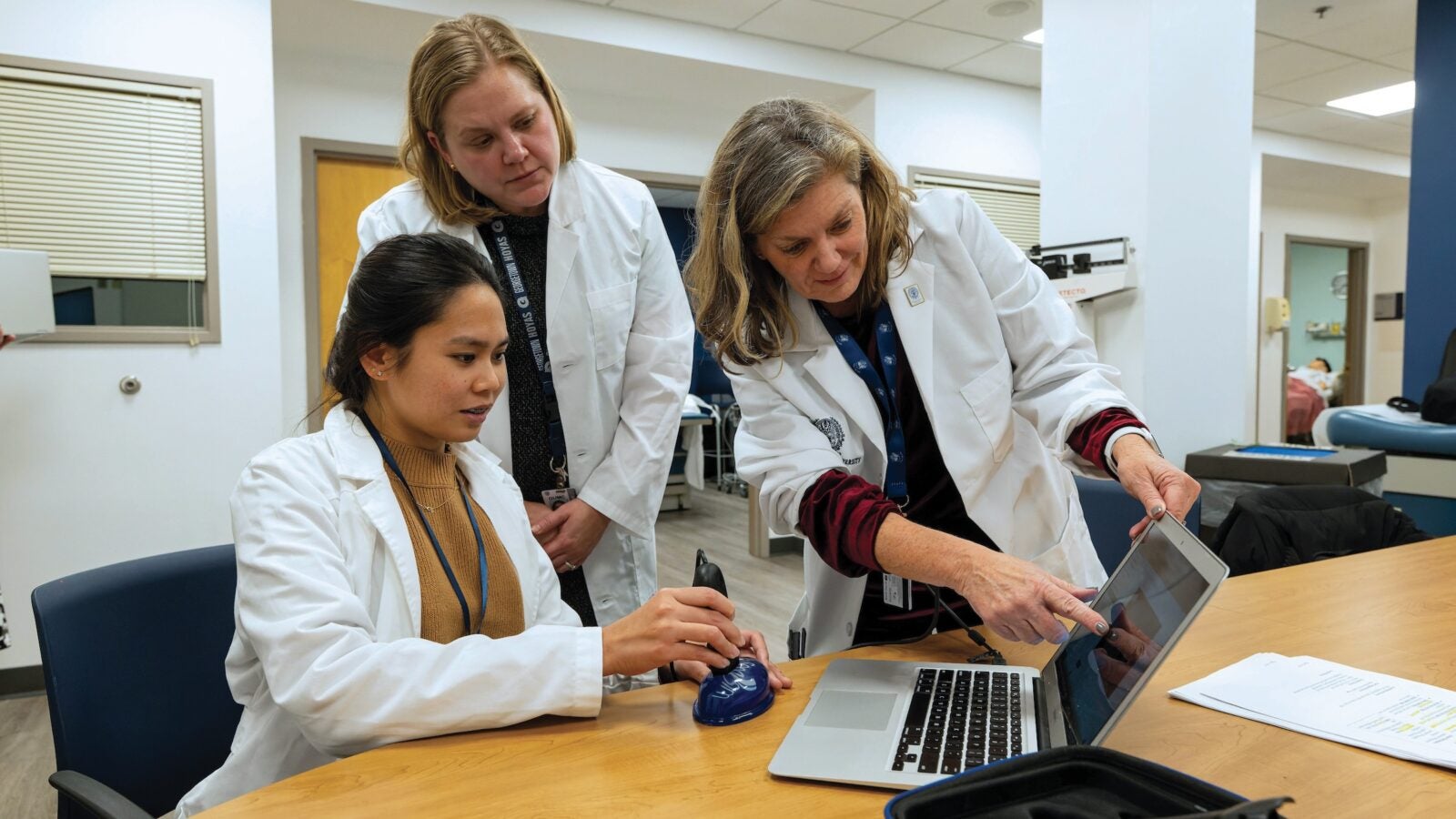 three people in white coats look at a laptop