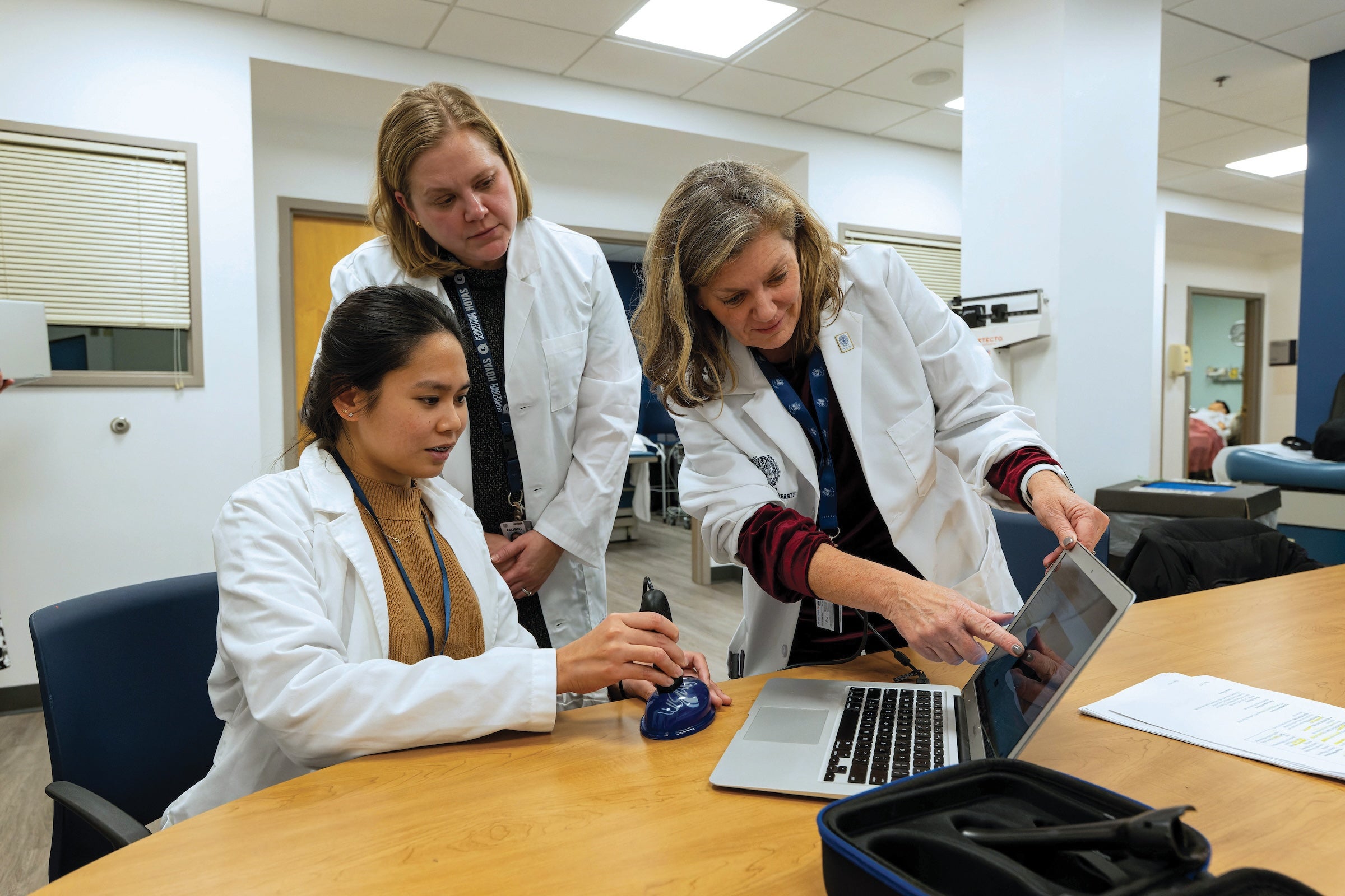 three people in white coats look at a laptop