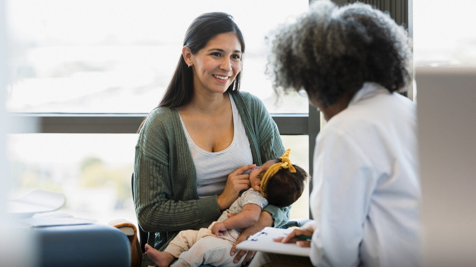 In the doctor's office, a mother smiles as medical worker gives her a positive report about her bay's medical exam