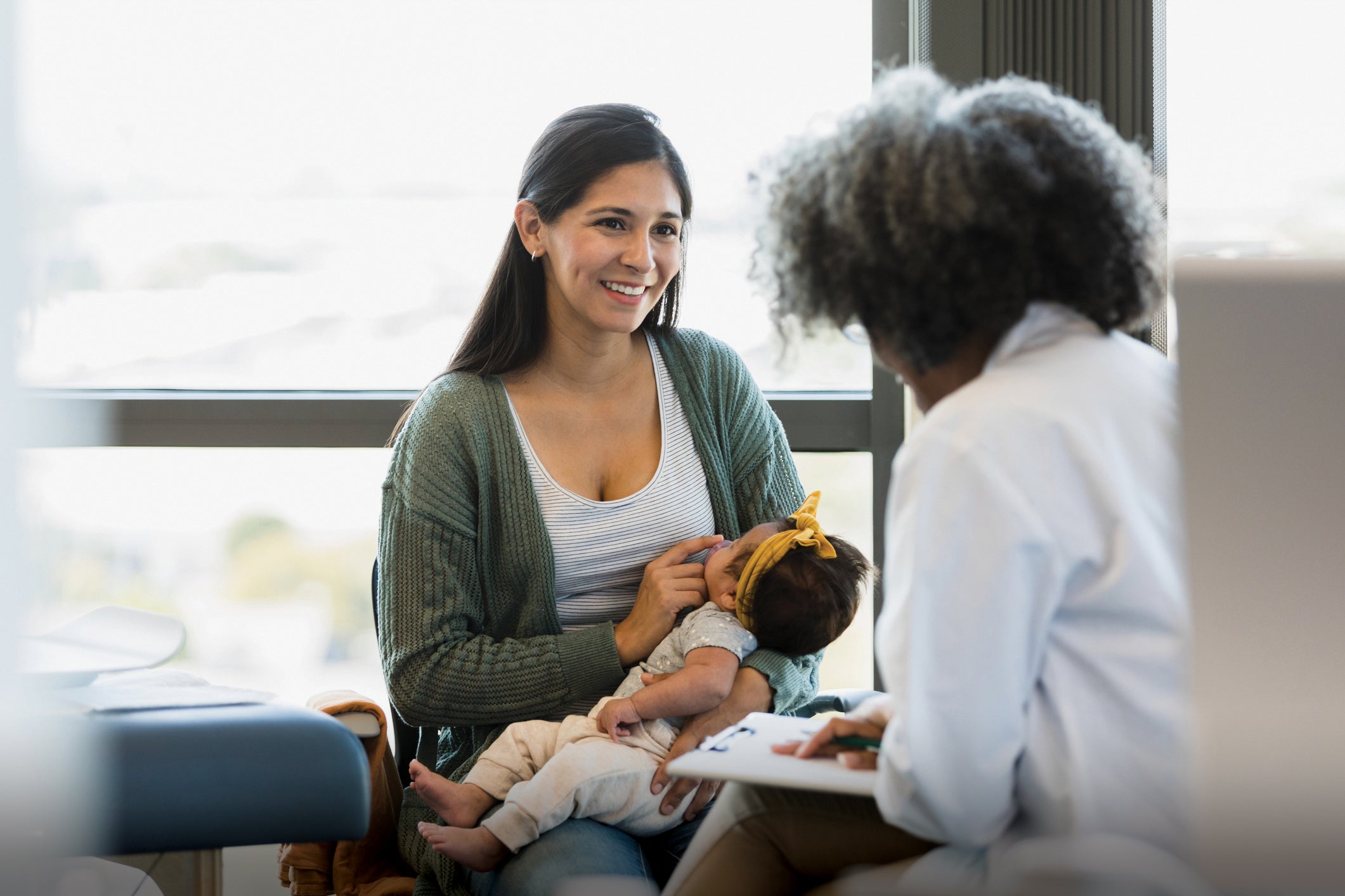 In the doctor's office, a mother smiles as medical worker gives her a positive report about her bay's medical exam