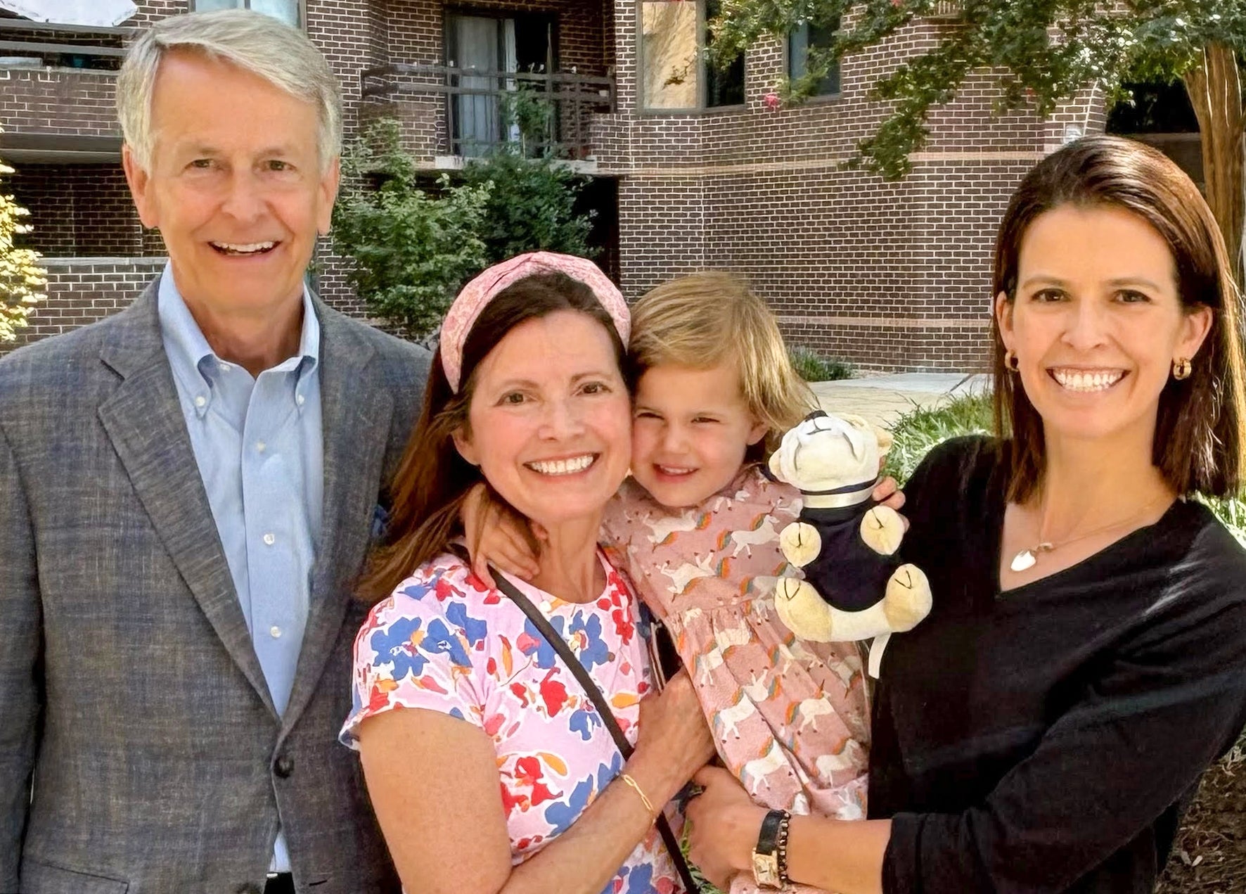 two women, a toddler and a man in a gray suit stand with each other