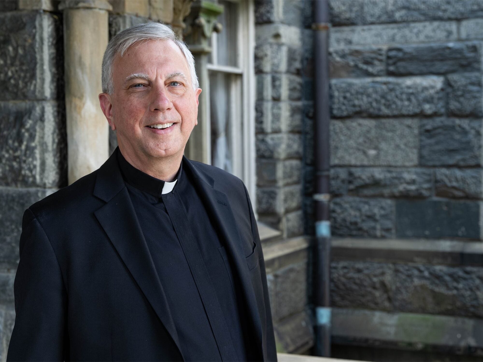 a man in clerical robes outside a gray stone building