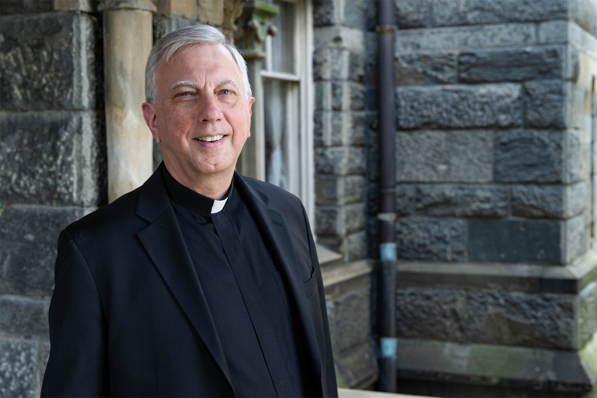 a man in clerical apparel outside of a gray stone building