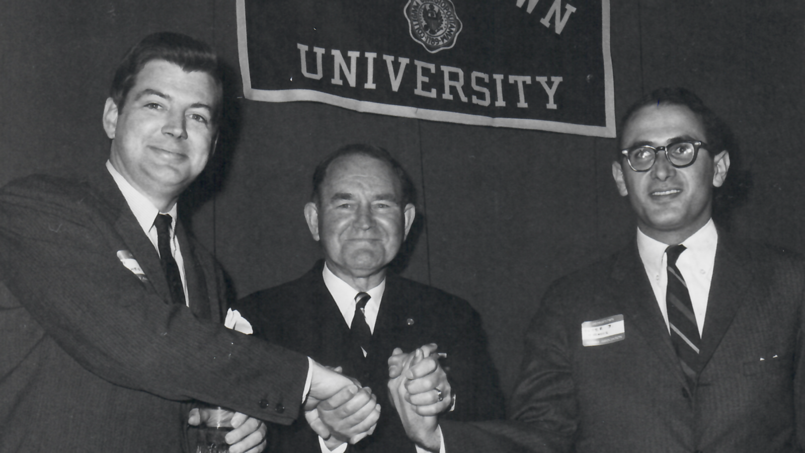 Three men shaking hands in front of Georgetown University banner.