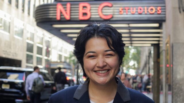a person smiles while standing outside of the 30 Rockefeller Plaza
