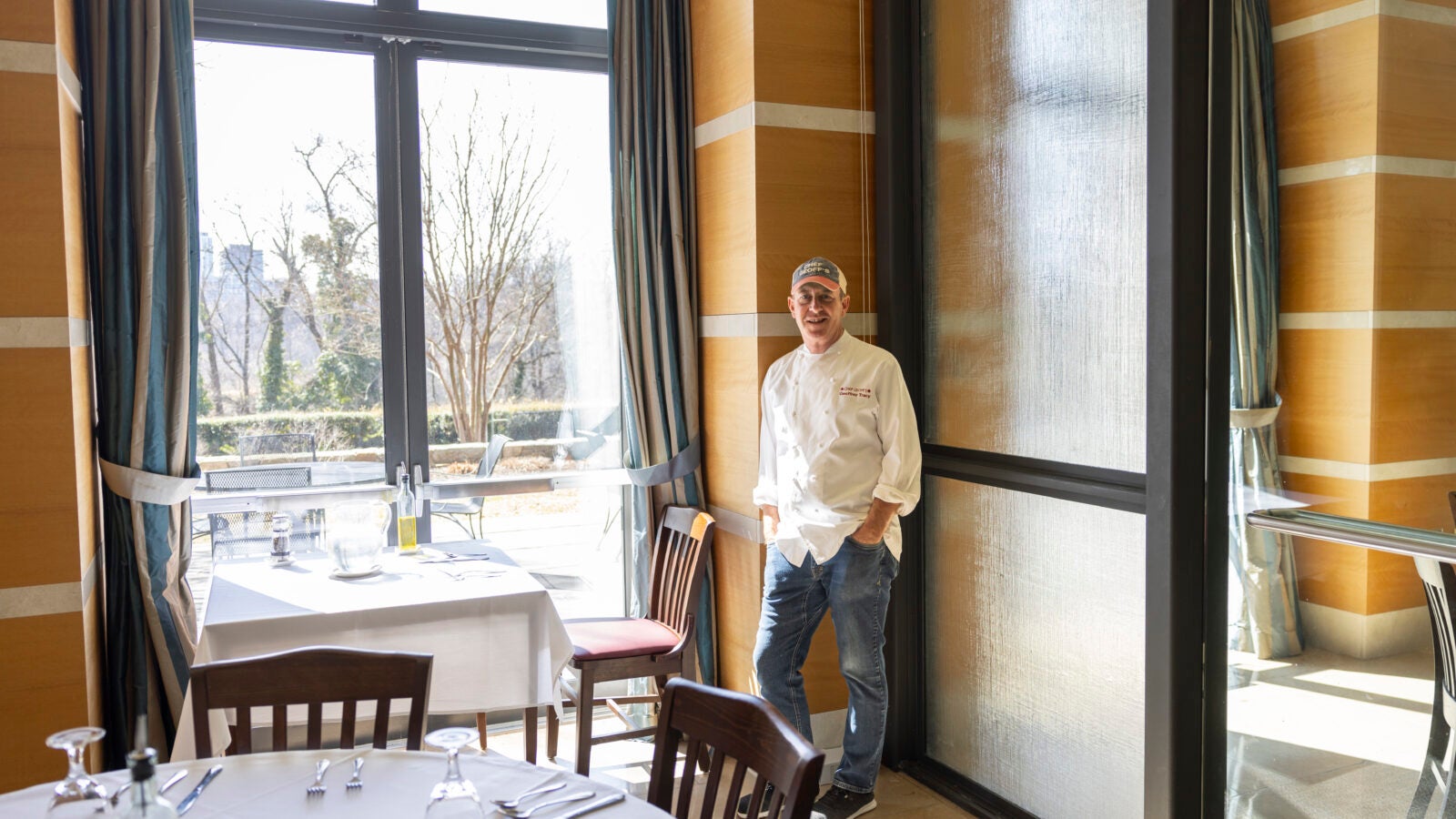 a man in a chef coat stands next to a window in a dining room