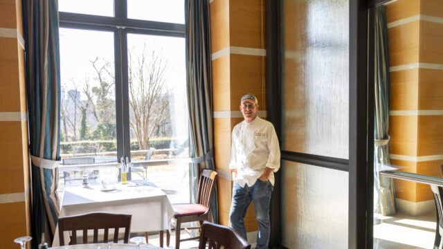 a man in a chef coat stands next to a window in a dining room