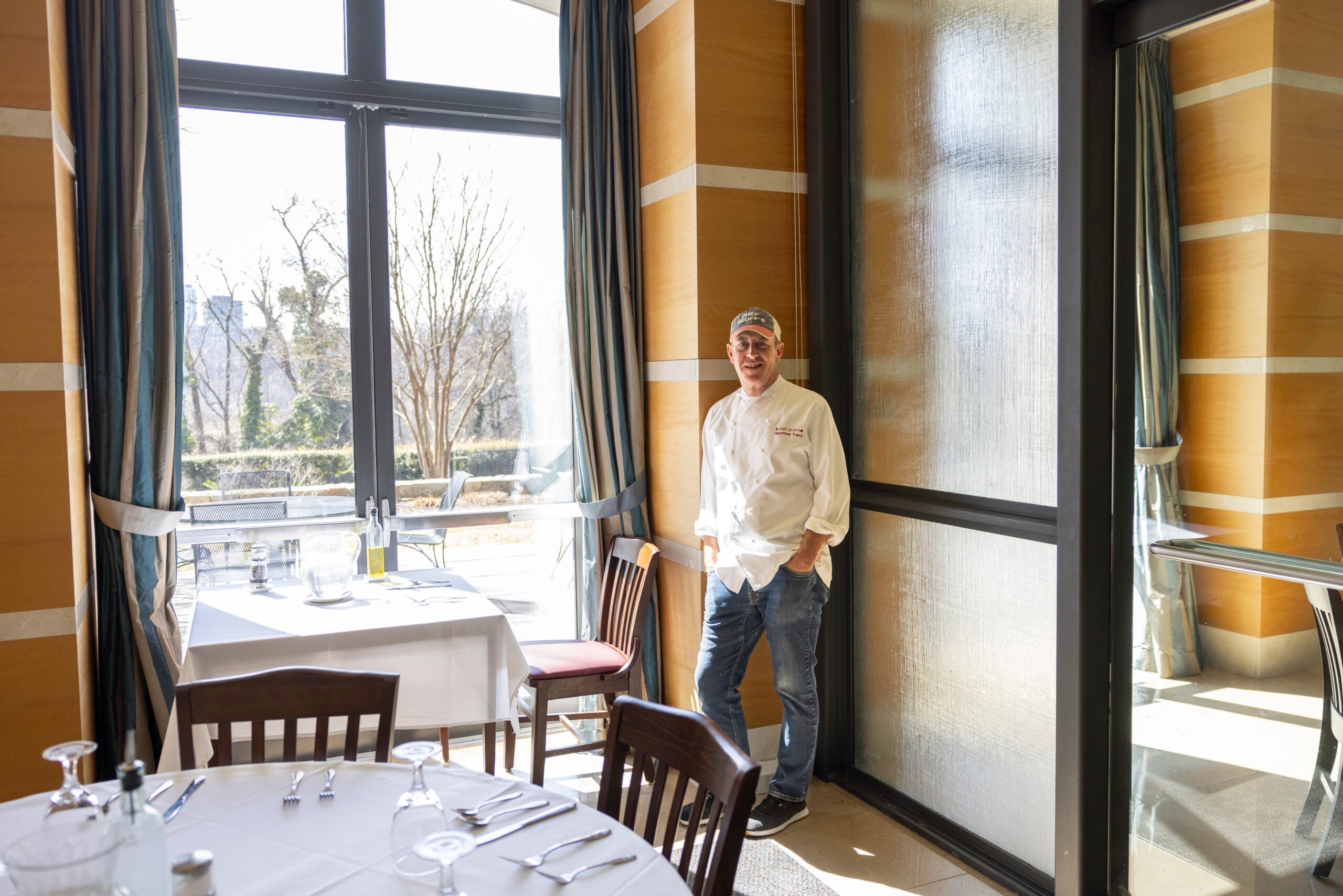a man in a chef coat stands next to a window in a dining room