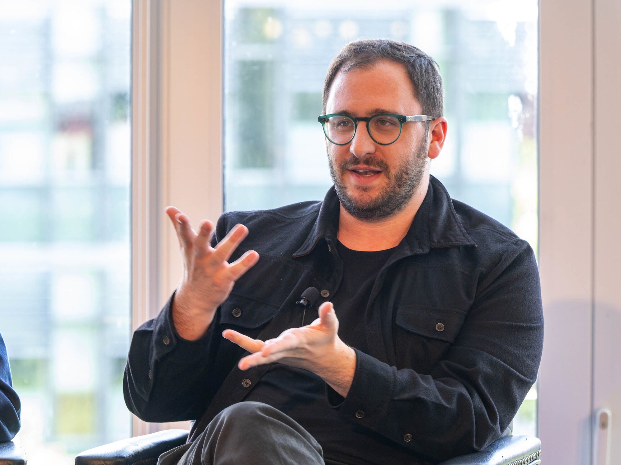 while sitting, a man with glasses gestures with his hands