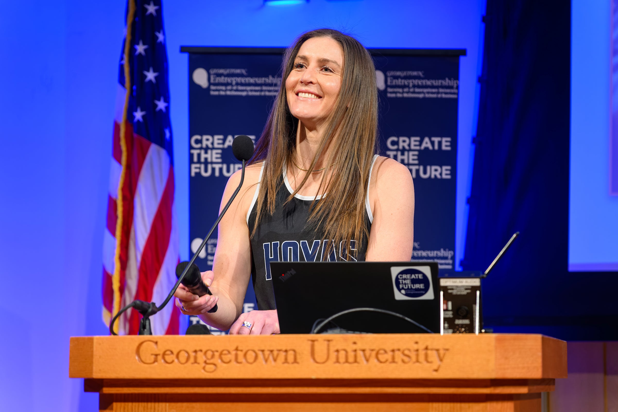 a woman stands at a podium and smiles
