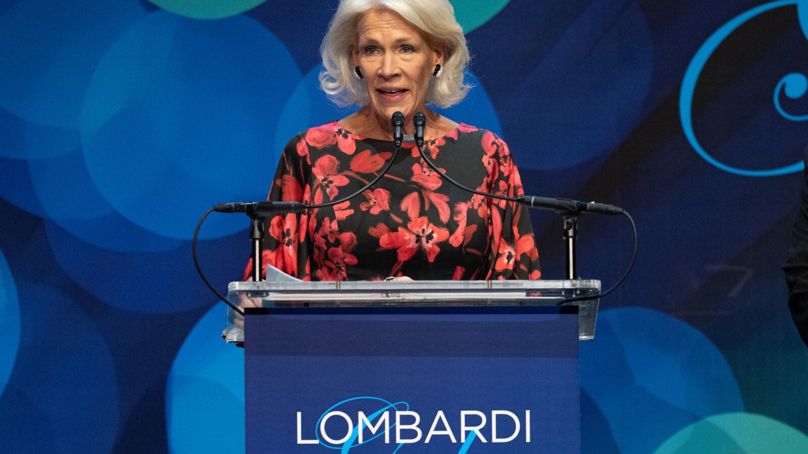 a woman in a black and red dress gives a speech at the Lombardi Gala podium