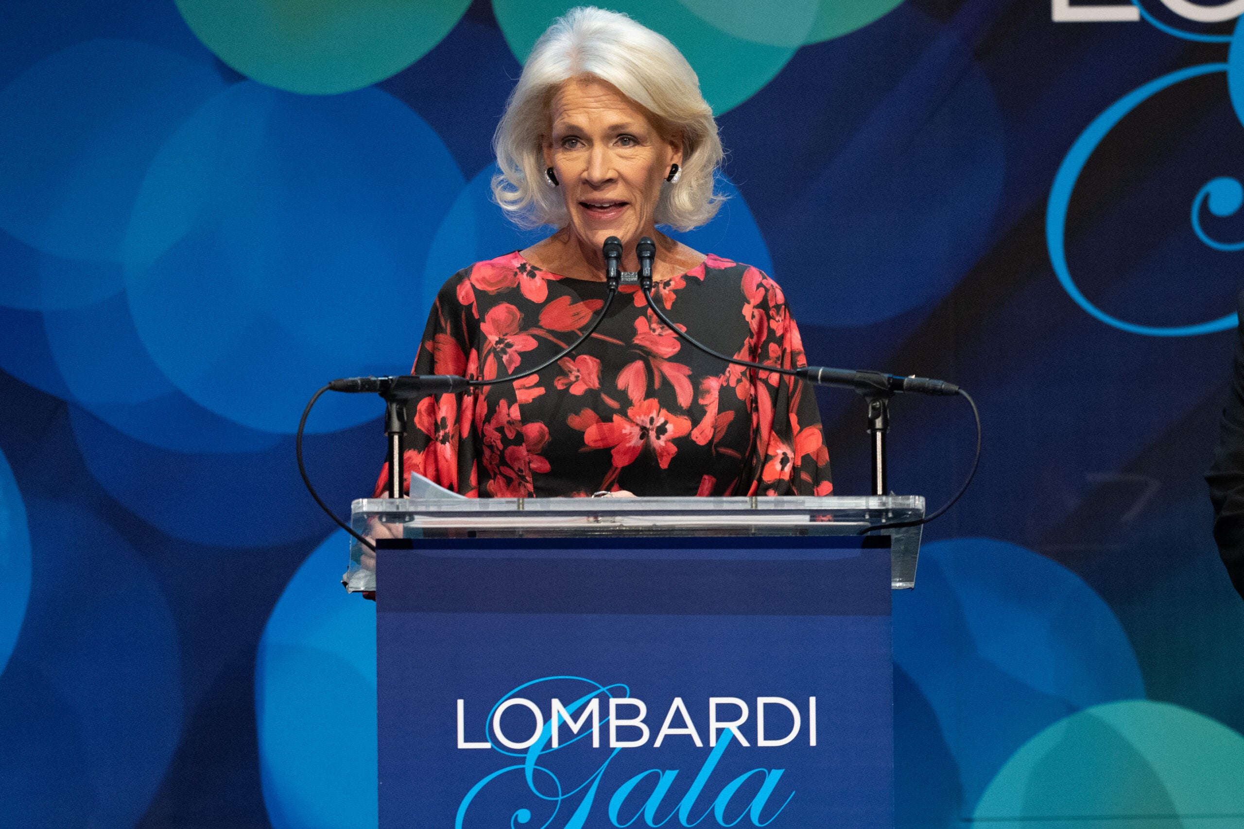 a woman in a black and red dress gives a speech at the Lombardi Gala podium