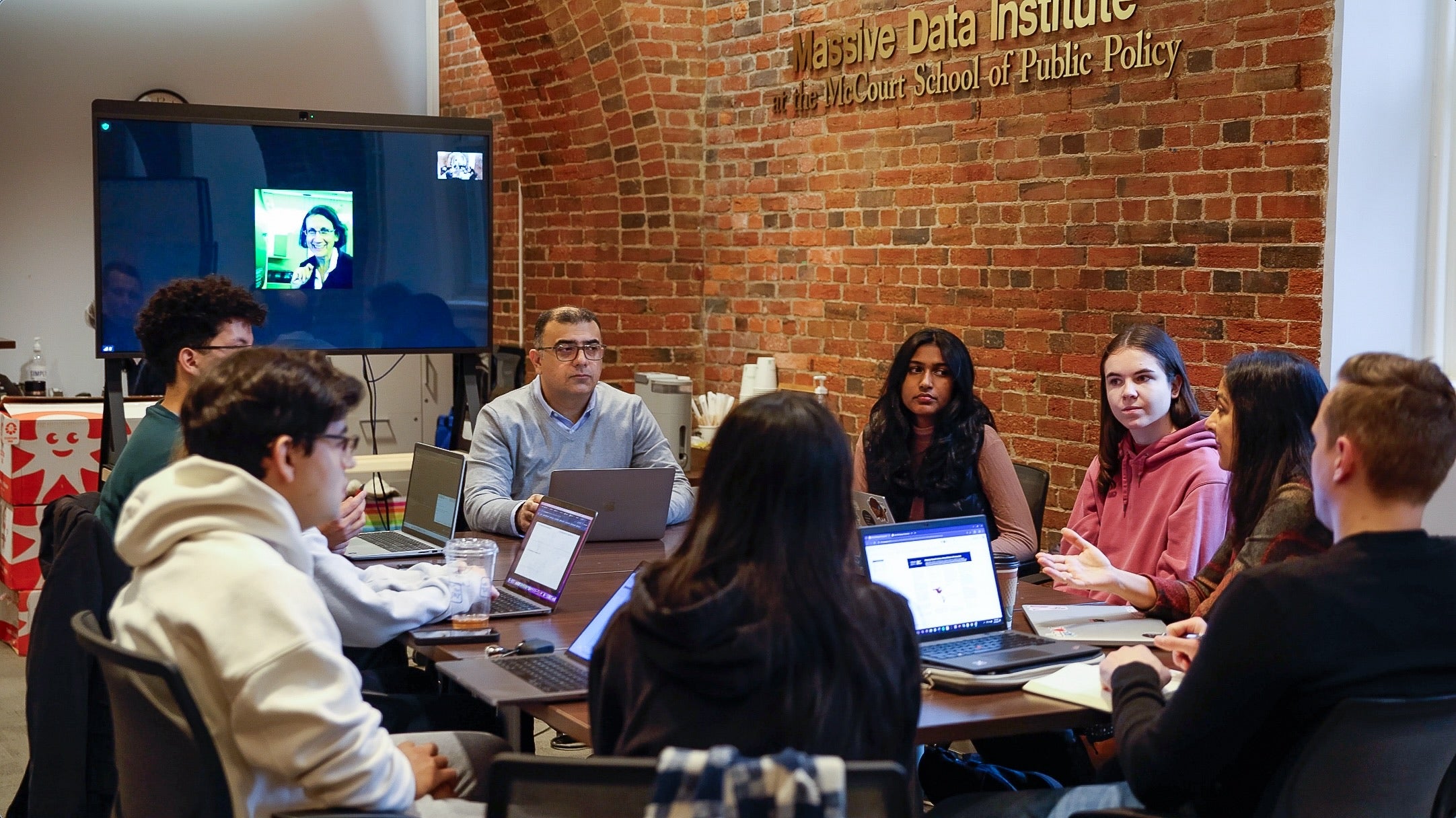 people sit around a table with the words "Massive Data Institute: at the McCourt School of Public Policy" on the wall